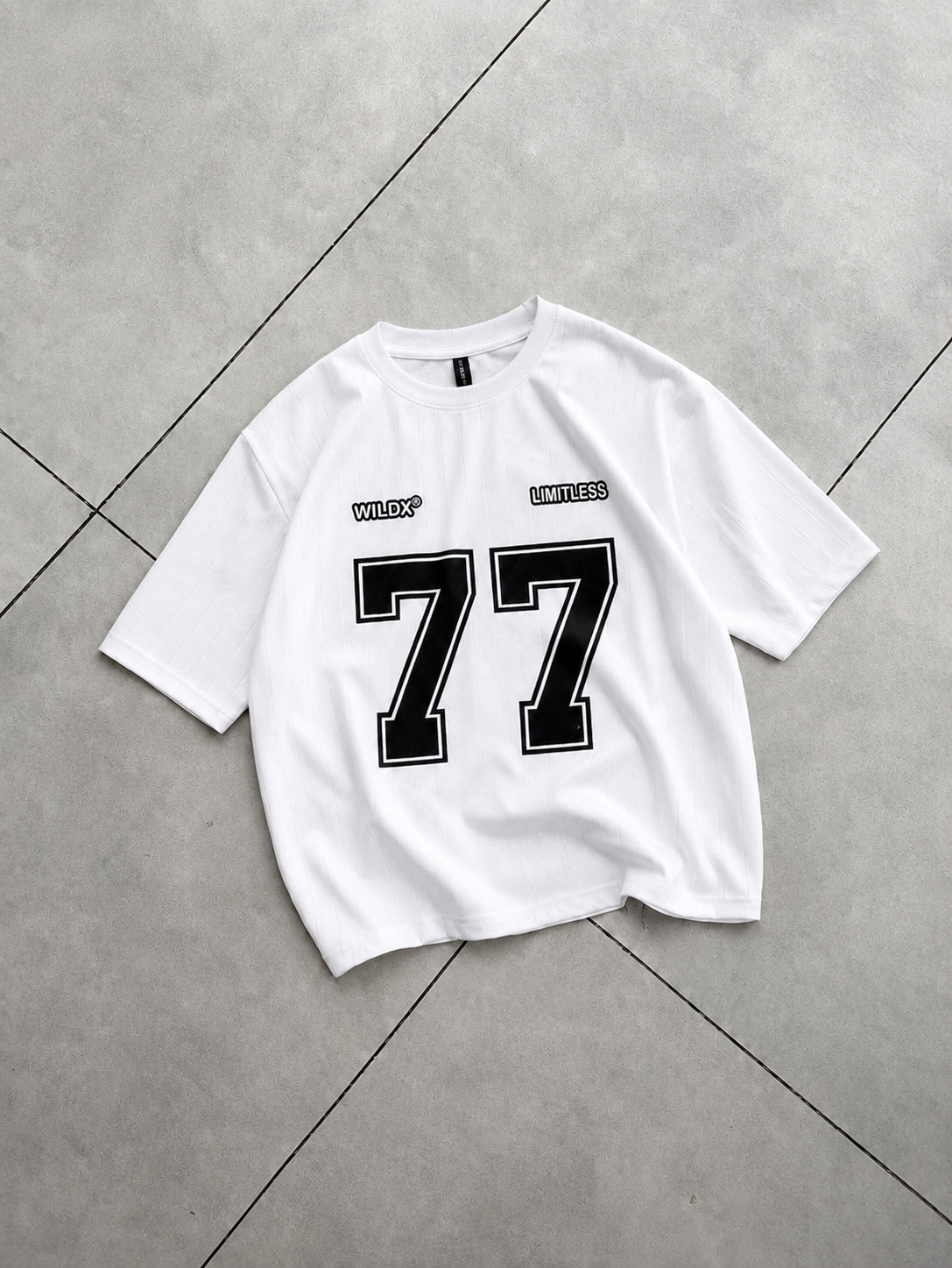 A white short-sleeve t-shirt with a large black and white number 77 on the front, laid flat on a gray tiled floor.