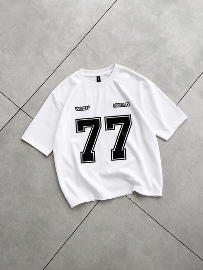A white short-sleeve t-shirt with a large black and white number 77 on the front, laid flat on a gray tiled floor.