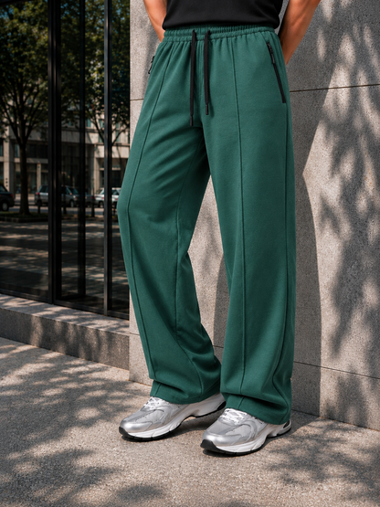A person wearing dark green wide-leg sweatpants with a black drawstring waist, standing outdoors against a stone wall.