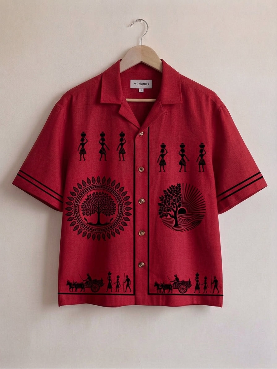 A red short-sleeve button-up shirt with black printed silhouettes of figures, circular tree motifs, and small cart scenes, hanging on a wooden hanger against a plain off-white wall.