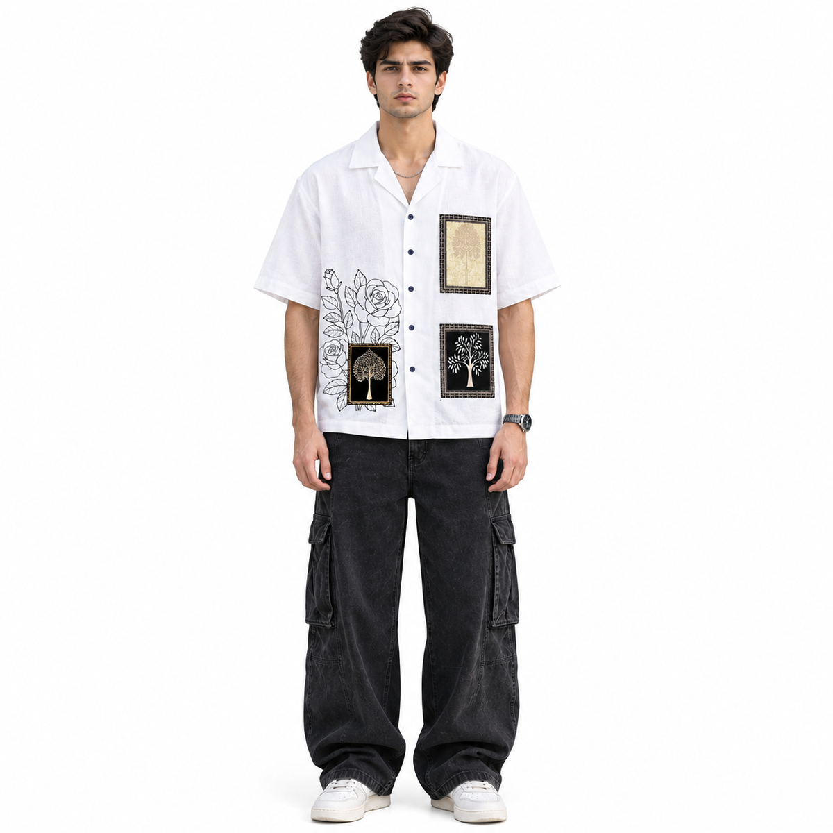 A man modeling a white short-sleeve button-up shirt with black and gold graphic prints, paired with black cargo pants and white sneakers, against a plain white background.